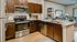Contemporary kitchen with elegant wooden cabinetry, stainless steel appliances, granite countertops, and hardwood flooring in an open-plan design leading to a cozy living area.