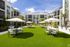 Luxurious apartment complex courtyard featuring modern outdoor seating, lush green lawn, and relaxing hammocks under sunny skies.