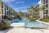 Luxurious apartment complex with modern architecture, featuring a sparkling swimming pool surrounded by lush palm trees and elegant lounging areas.