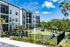 Modern apartment building with balconies, surrounded by lush greenery and featuring a fenced pet walk area under a clear blue sky.
