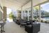 Luxurious outdoor patio with modern wicker furniture overlooking a sparkling pool and lush palm trees.