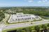 Aerial view of a contemporary apartment complex surrounded by lush greenery and waterways, offering scenic living with convenient road access.