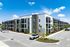 Modern three-story apartment complex with stylish balconies and palm tree landscaping, featuring ample parking and set against a vibrant blue sky.