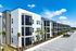 Modern apartment complex with sleek architecture and palm trees, offering ample parking and vibrant living spaces against a clear blue sky.