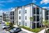Modern apartment complex with sleek architecture, sunny balconies, and lush landscaping on a bright day.