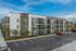 Contemporary apartment complex featuring modern architecture with large windows and spacious balconies, surrounded by lush landscaping and ample parking space.