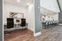 Modern open workspace with sleek desks and ergonomic chairs, leading to an elegant kitchen bar area with stylish lighting and ample seating.