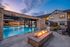 Inviting apartment complex featuring a sparkling swimming pool with lounging chairs and umbrellas, surrounded by modern two-story buildings under night time sky.