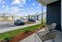 Charming apartment patio view with stylish outdoor seating, overlooking a modern parking area with sleek cars and well-maintained landscape under a bright blue sky.