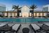 Luxurious apartment complex featuring a sparkling outdoor pool flanked by stylish loungers and elegant palm trees, creating a perfect oasis for relaxation.
