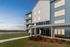 Contemporary apartment building with elegant balconies overlooking a serene water view at sunset, surrounded by lush landscaping.