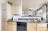 Bright kitchen with light wood cabinets, granite countertops, and a view into a stylish living area.