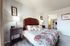 Charming bedroom with a floral bedspread, elegant lamps, and tasteful wall art, leading to an en suite bathroom.