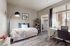 Bright bedroom featuring a cozy bed with blue accent pillows, a modern lamp, a workspace, and an elegant wood floor.