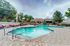 Luxurious outdoor pool area featuring modern lounge chairs, surrounded by lush greenery and a stylish clubhouse backdrop.