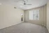Bright and airy living room with plush carpeting, large window with a ceiling fan.