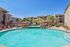 Luxurious apartment complex with a sparkling outdoor pool, lounge chairs, and lush greenery, perfect for relaxation and leisure.