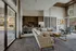 Elegant open-plan living space featuring a cozy sectional sofa, modern kitchenette, and expansive glass doors leading to an outdoor fireplace area.