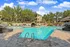 Gorgeous outdoor swimming pool area with stylish lounge chairs, surrounded by lush greenery and upscale apartments under a vibrant blue sky.