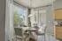 Bright dining area with elegant table set for four, large windows offering scenic outdoor views, and sliding glass doors leading to cozy patio seating.