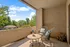 Charming apartment balcony with cozy seating, vibrant plant decor, and scenic views of lush greenery and blue skies.