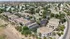 Aerial view of a modern apartment complex with beige rooftops, lush greenery, and ample parking, situated on the edge of a scenic desert landscape.