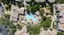 Stunning aerial view of a luxurious apartment complex featuring an expansive resort-style pool, lush greenery, and spacious outdoor amenities.