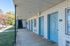 Delightful apartment exterior with white brick walls and blue doors, featuring a well-maintained walkway and lush greenery.