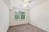 Bright and airy bedroom with a large window offering serene views of green trees, featuring soft carpeted flooring and a modern ceiling fan.