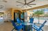 Inviting outdoor lounge area with vibrant blue chairs and a ceiling fan, overlooking a sparkling pool through elegant fencing.