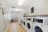 Bright laundry room featuring multiple washers and dryers, modern lighting, and comfortable seating area by the window.