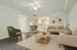 Bright and inviting living room with modern decor, featuring a cozy seating area, stylish green accent chair, and open access to a sleek kitchen and dining area.