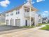 Charming two-story apartment building with modern design, featuring three garages, elegant white siding, and a welcoming staircase, set against a clear blue sky.