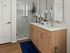 Elegant bathroom featuring dual sinks with a sleek wooden vanity, modern faucet fixtures, and a glass-enclosed shower, accented by decorative candles and an orchid for a touch of luxury.