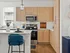 Chic modern kitchen with light wood cabinets, stainless steel appliances, and a cozy breakfast bar featuring a plush blue chair.