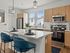 Modern kitchen with sleek white countertops, stylish wooden cabinets, stainless steel appliances, and elegant blue chairs at the island.