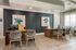 Modern office space with sleek wooden desks, stylish woven chairs, and contemporary plant artwork for a professional and inviting atmosphere.