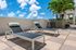 Luxurious rooftop patio with modern lounge chairs, tropical plants, and vibrant blue skies, perfect for relaxation.