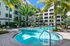 Luxurious apartment complex with a stunning resort-style pool, surrounded by lush palm trees and modern lounging areas.