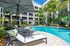 Luxurious apartment complex with a pristine pool, surrounded by lush tropical landscaping and contemporary architecture.