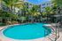 Elegant apartment complex with a sparkling blue pool surrounded by lush palm trees and modern balconies, perfect for relaxation and leisure.