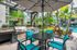 Luxurious outdoor patio featuring a sleek BBQ area, stylish seating with turquoise chairs, and a vibrant poolside view surrounded by lush palm trees.