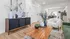 Chic modern living room with elegant decor, featuring a sleek wooden coffee table, plush white armchair, and stylish artwork; open layout flows into a contemporary kitchen, creating a cozy and inviting atmosphere.