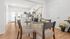Bright and inviting dining area with a modern glass table, elegantly set for four, leading into a sleek, open kitchen with contemporary finishes.