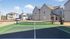 Charming suburban community with modern homes featuring a tennis court surrounded by fresh landscaping under a bright blue sky.