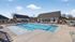 Inviting outdoor pool area with modern sun loungers and charming clubhouse under a bright blue sky.
