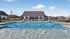 Luxurious outdoor pool area with sparkling water, surrounded by chic lounge chairs and a stylish clubhouse under a clear blue sky.
