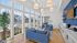 Bright and inviting lounge area featuring cozy blue sofas, decorative pendant lighting, large windows overlooking a sparkling pool, and a modern refreshment bar.