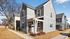 Charming modern townhouse with elegant gray siding, surrounded by a tidy lawn and mature trees, perfect for serene living.