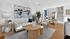 Chic living room featuring a cozy beige sofa, stylish abstract artwork, and vibrant greenery, leading to a sunlit dining area with elegant decor and modern stairs.